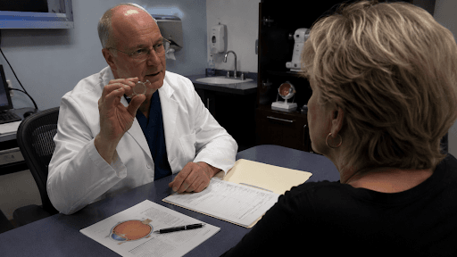 An eye surgeon holds up a multifocal intraocular lens demo model during a cataract surgery consultation with a patient in Louisville, KY.