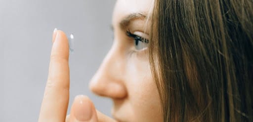 A young woman focuses intently as she applies a contact lens, close-up shot highlighting her eye and careful fingers.
